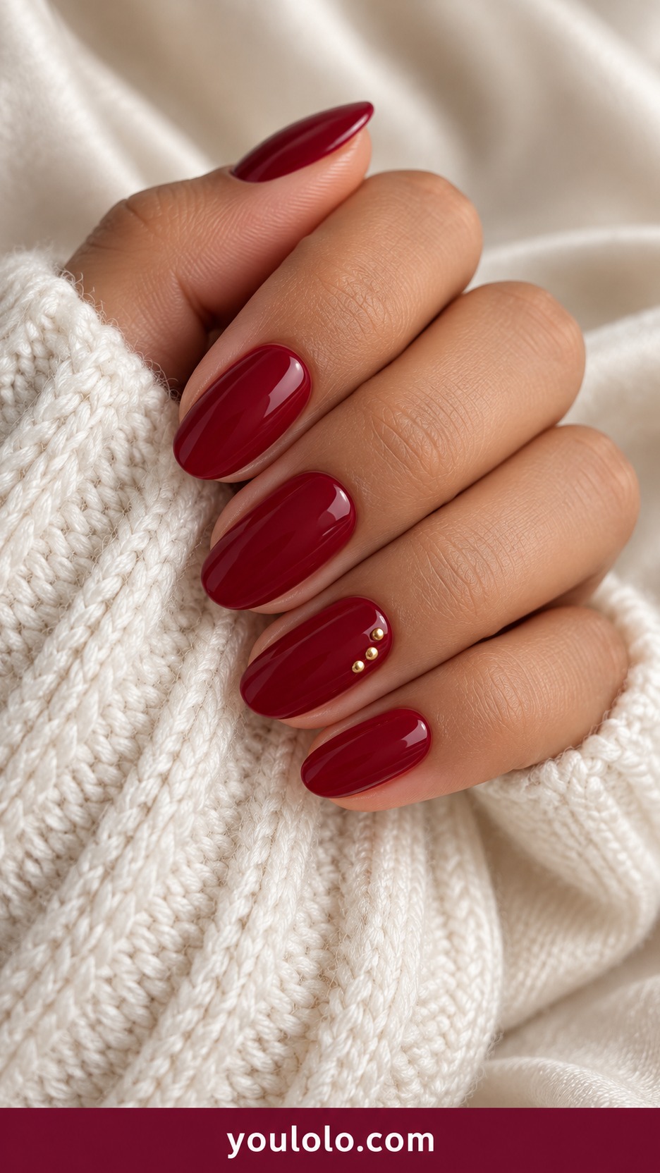 Short almond wine red glossy nails with three tiny gold dots near side of one accent on a naturally curled young adult hand