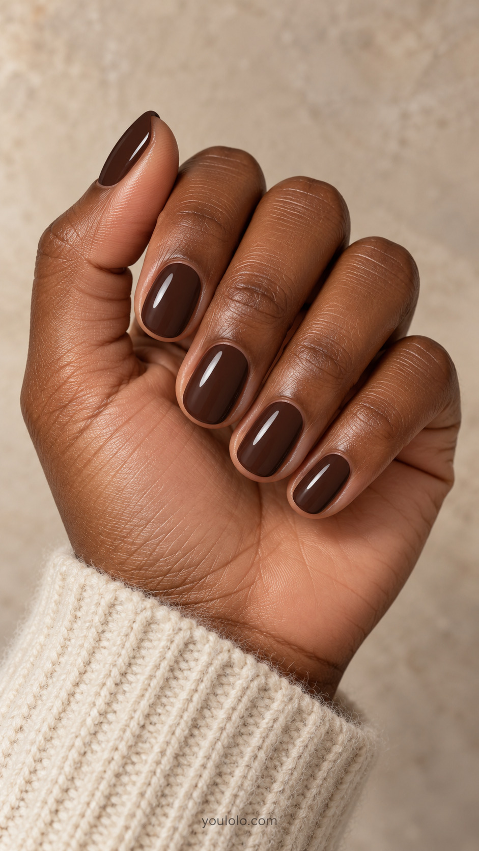 Short round nails with glossy espresso brown polish beside an ivory wool cuff.