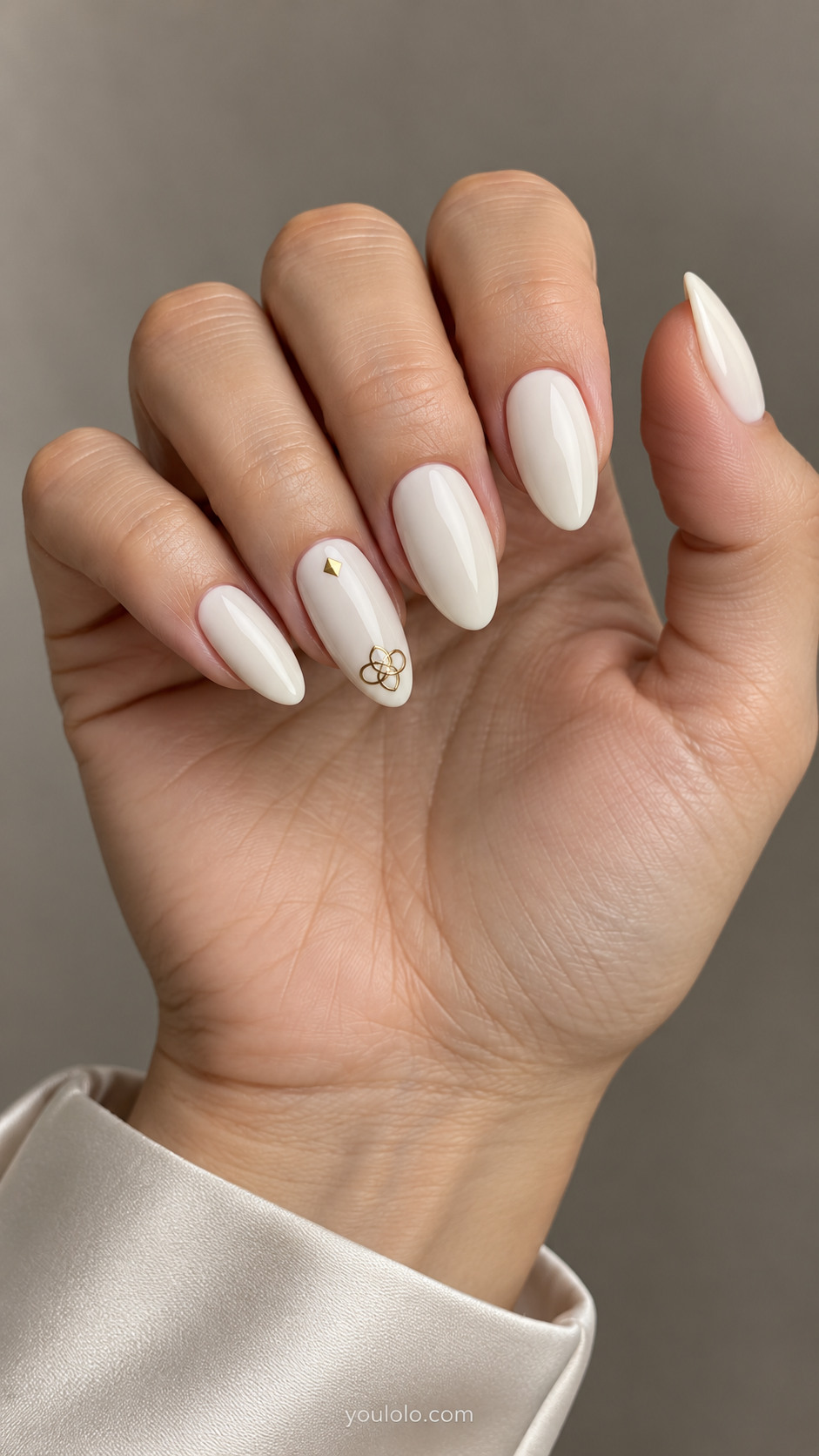 Medium almond ivory nails with a small interlaced gold knot near the ring-nail tip and a tiny gold square near its cuticle