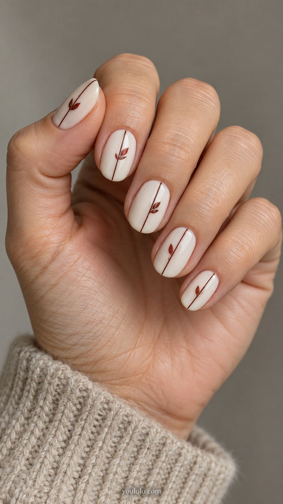 Short oval nails with ivory nails with single thin vertical chocolate pinstripe on each; tiny brick red leaf attached at different heights, flat simple motif.
