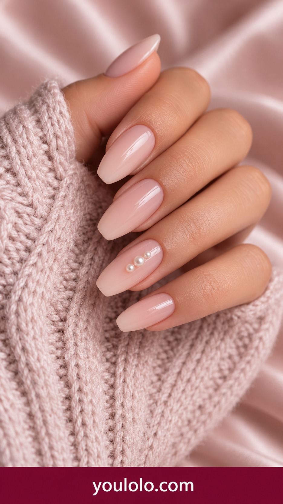 Medium oval creamy nude nails with a single vertical row of three tiny ivory pearls on one accent only on a naturally curled young adult hand