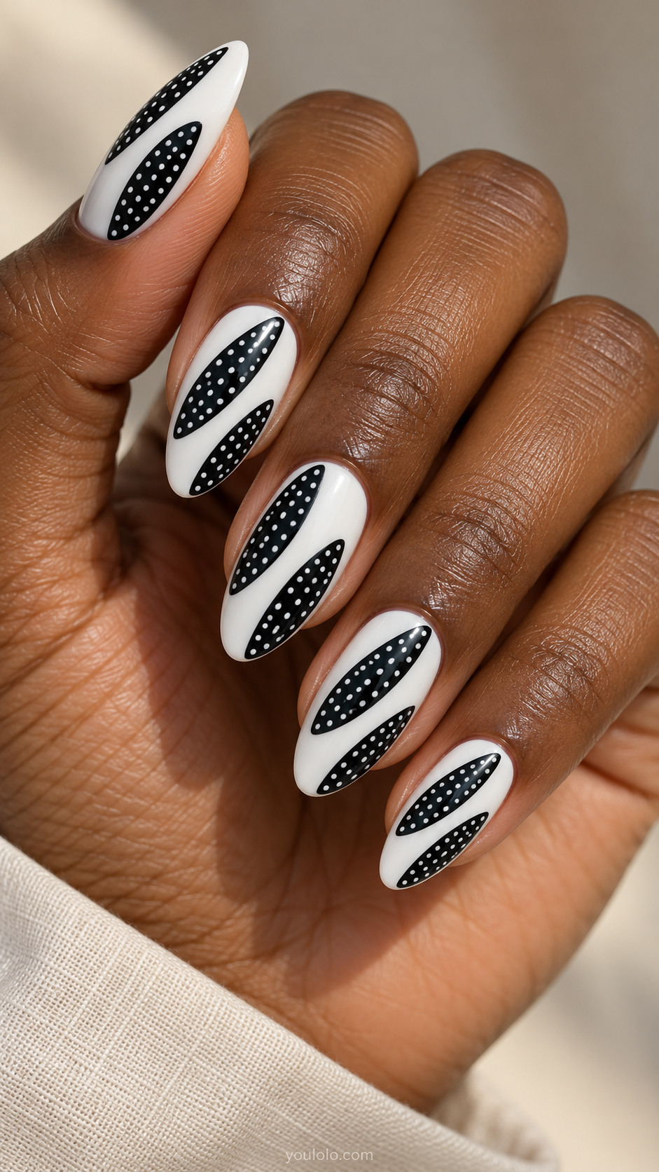 Medium almond white nails with two elongated narrow black oval islands placed diagonally each filled tiny white dots, separated by white gap
