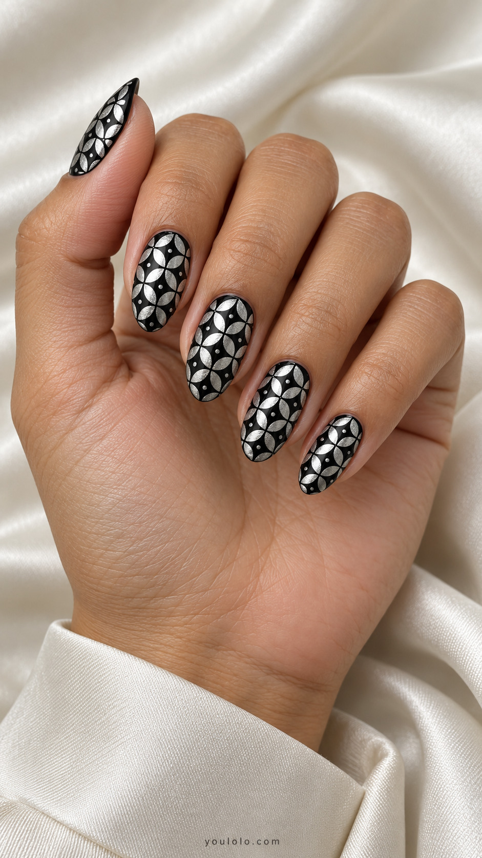 Black almond nails with a repeating metallic silver four-petal tile pattern and small silver dots