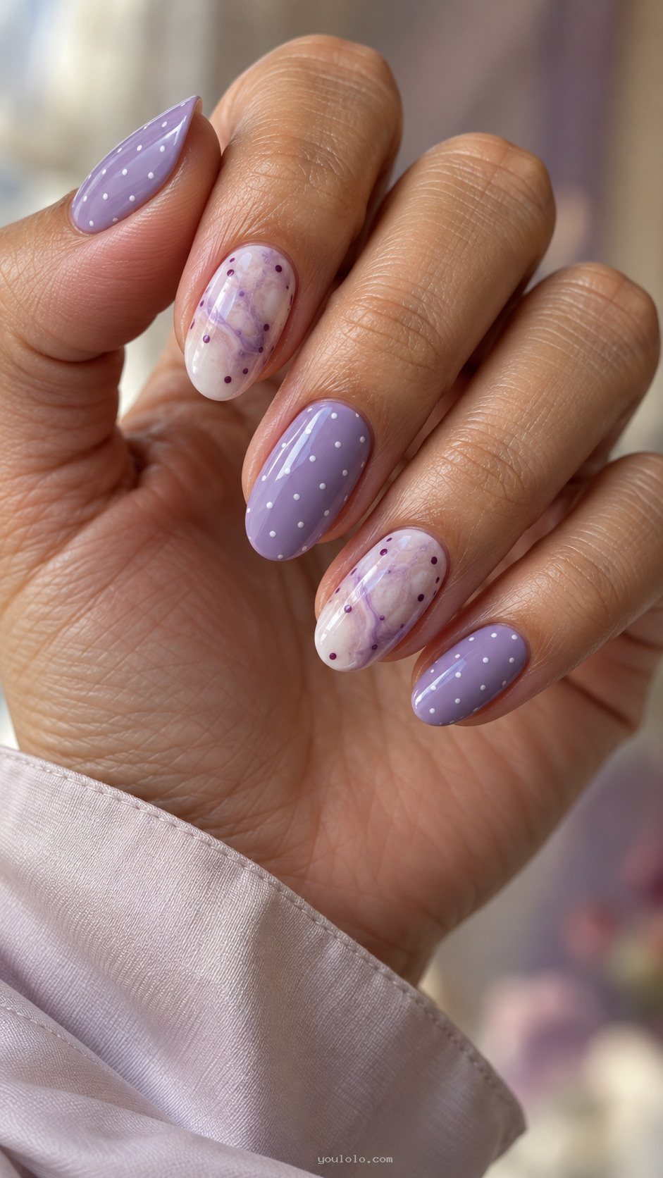 Lavender oval nails with white pin dots and cloudy marble accents.