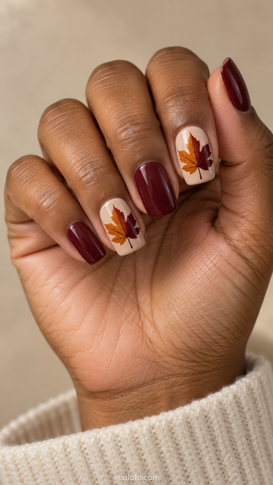 Medium square nails with soft beige nails with large maple silhouette on ring and index, each leaf split vertically burnt orange and burgundy; other nails plain muted burgundy.
