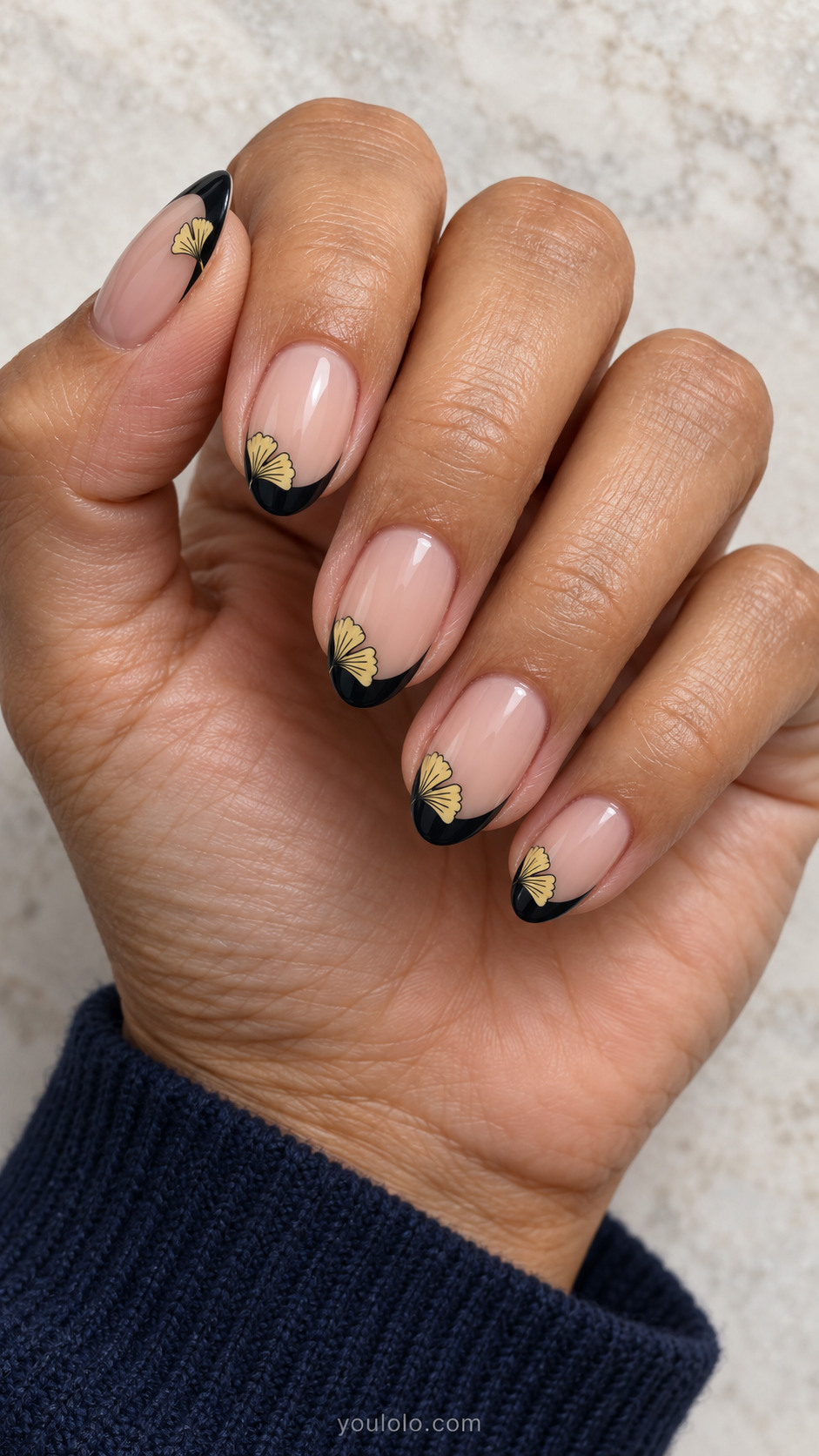 Medium almond nails with sheer nude nails with fine black French tips; tiny pale yellow flat ginkgo fan at one side of each tip, fine black radial strokes.