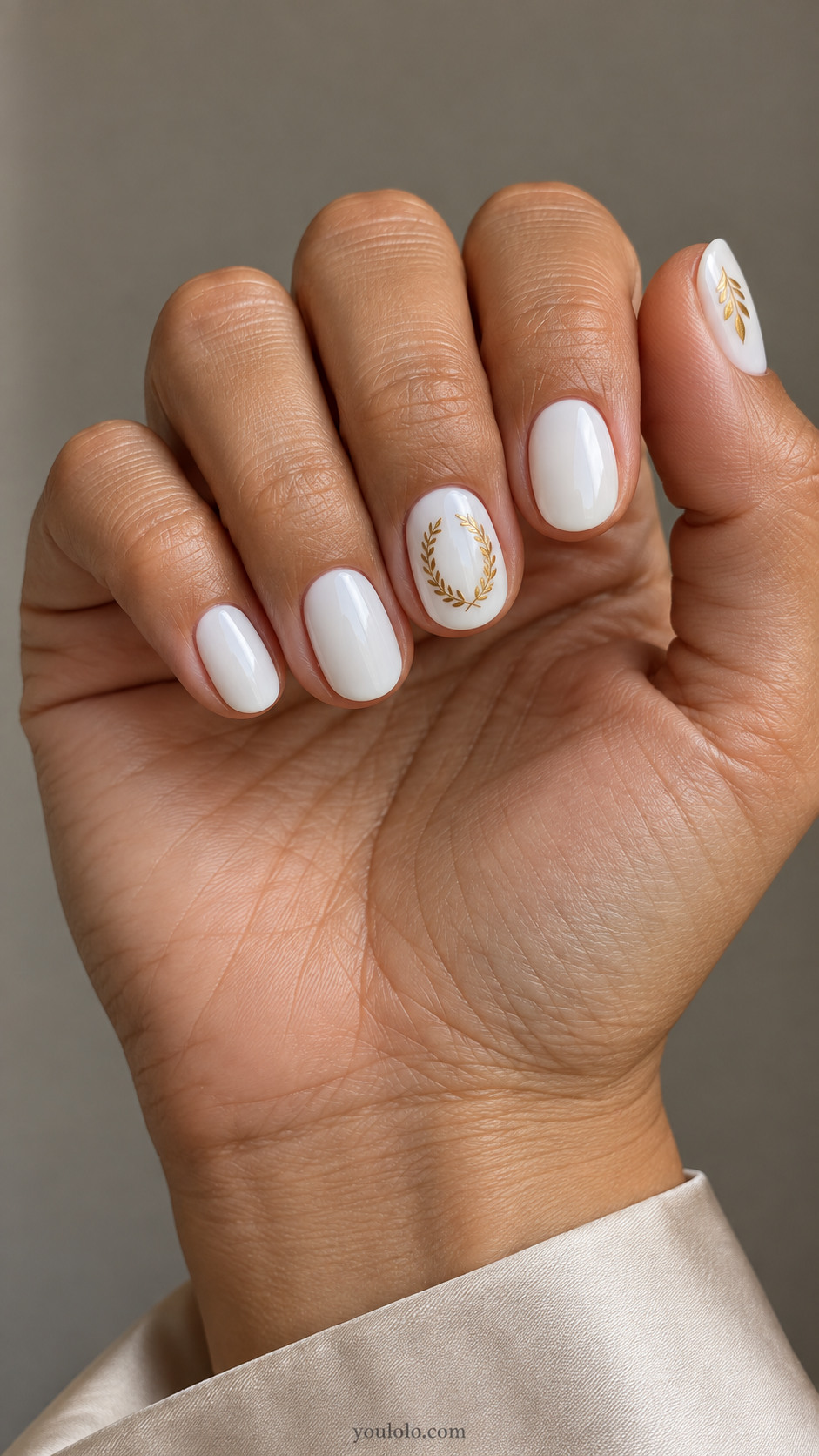 Short oval white nails with a miniature gold laurel wreath on the middle nail and a thumb leaf detail