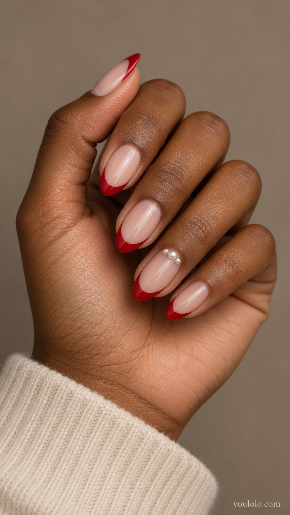 medium almond nude nails, classic red tips, three tiny low-profile seed pearls near ring nail cuticle only on a naturally gathered hand