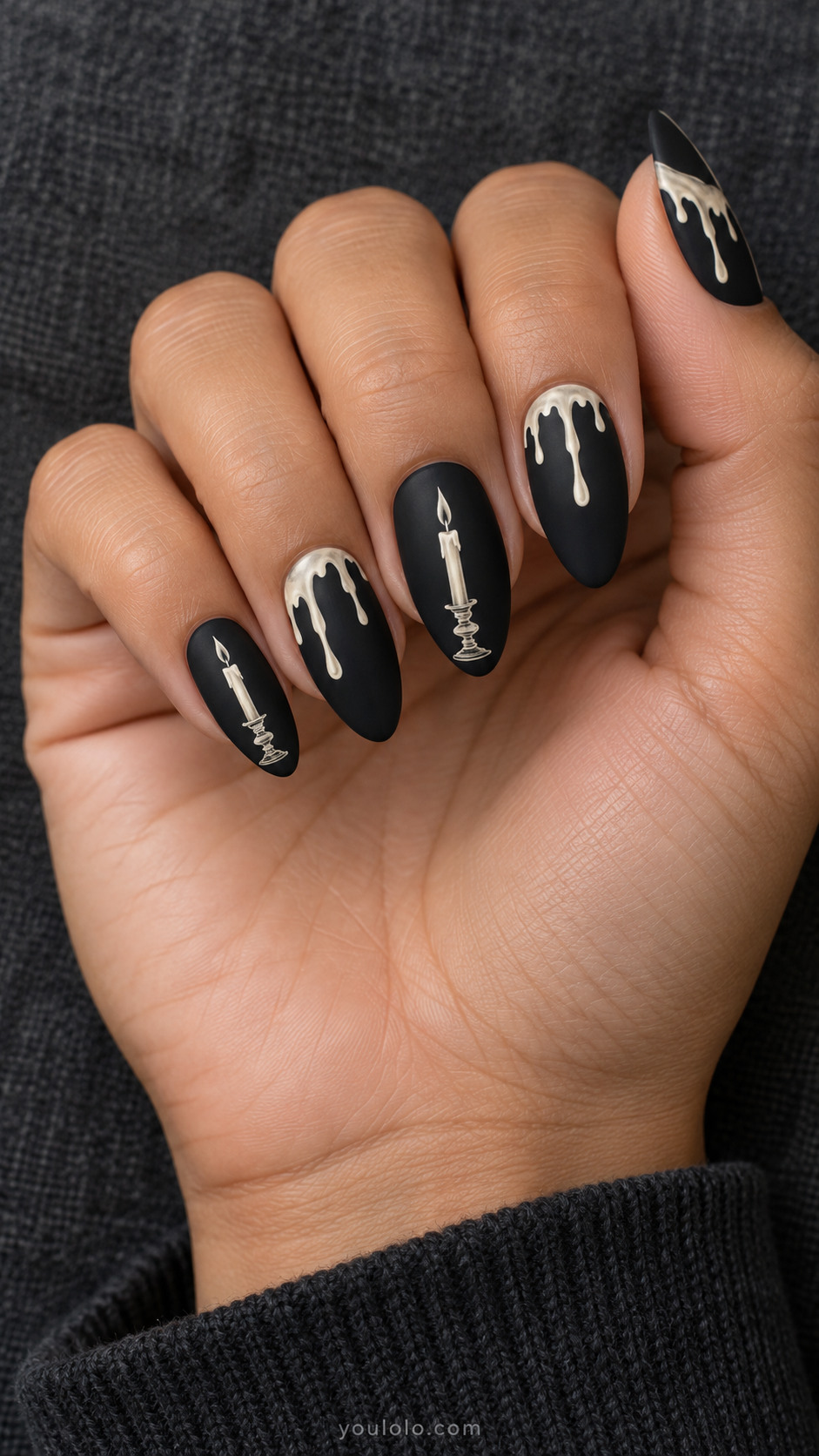 Medium almond matte black nails offwhite wax-drip shapes descending asymmetrically from cuticles on three fingers and fine slim ivory candlestick on two