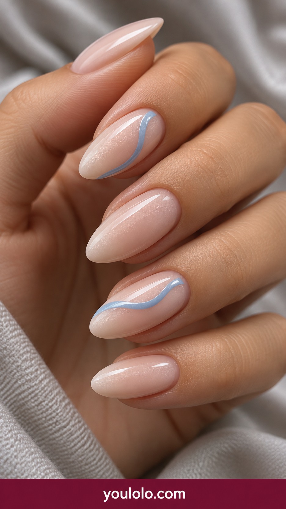 Medium oval milky nude nails with one fine powder blue flowing ribbon line across two accents, rest plain pearly nude on a naturally curled young adult hand