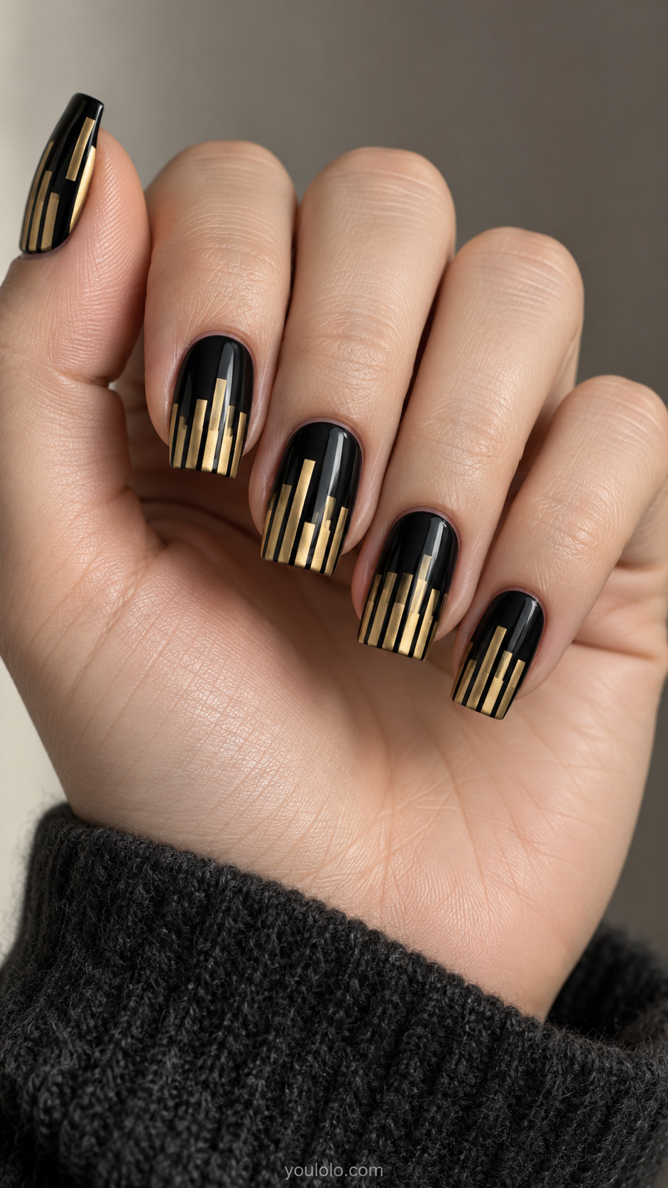 Black tapered square nails with gold piano-key bars extending from the tips