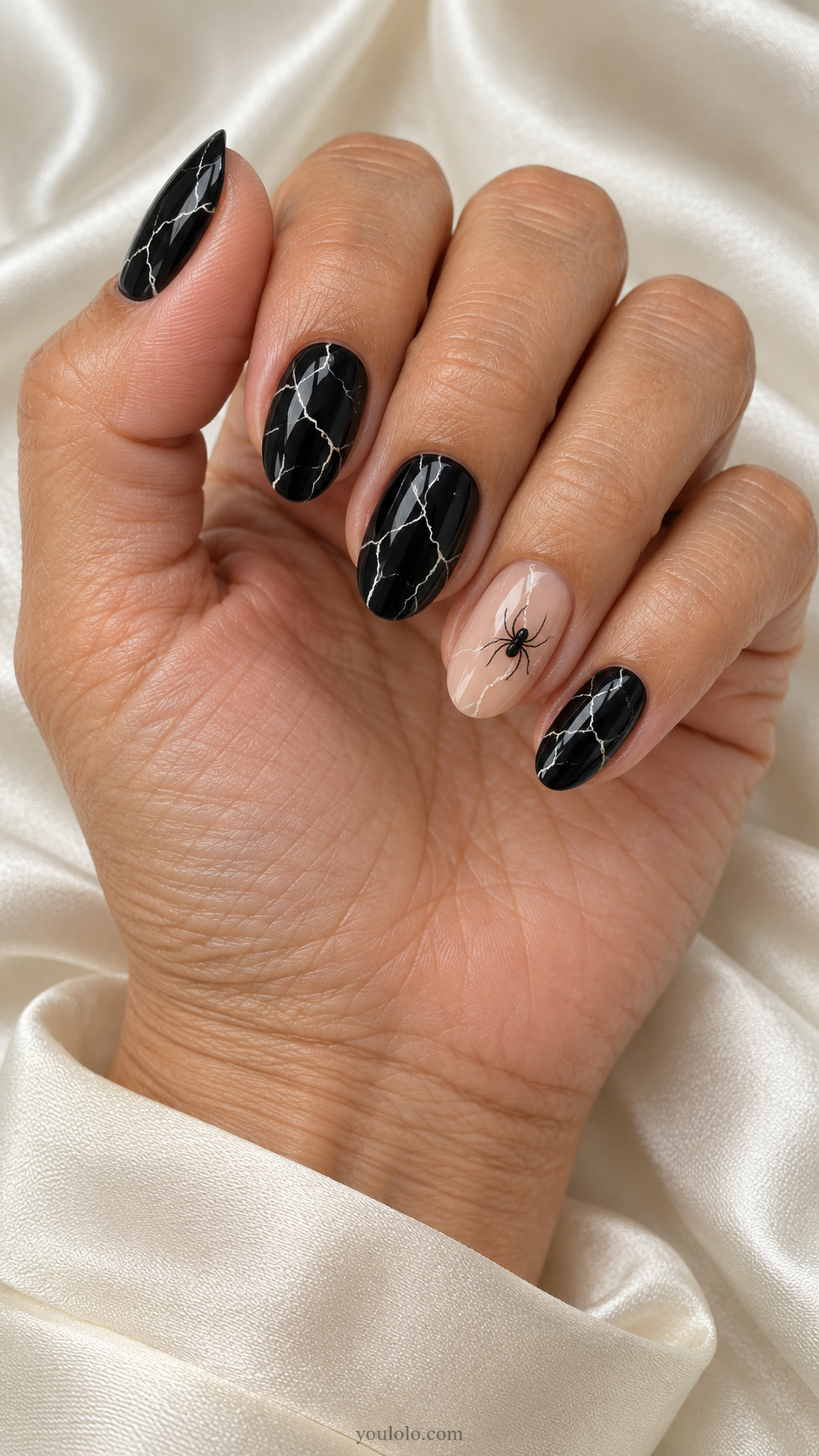 Medium oval black nails irregular very fine bone-white lightning crack lines across black with one tiny spider silhouette on neutral translucent accent nail