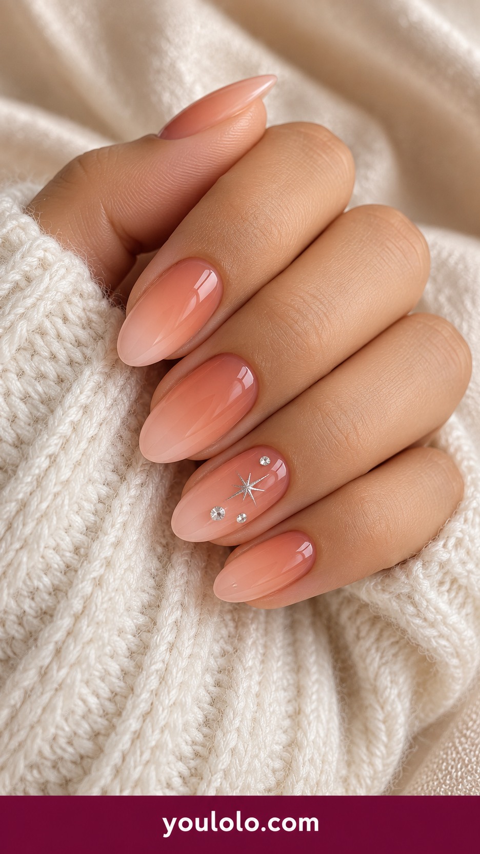 Medium almond sheer peach pink nails with three tiny flat clear crystals placed asymmetrically on one accent and a tiny silver painted star on a naturally curled young adult hand
