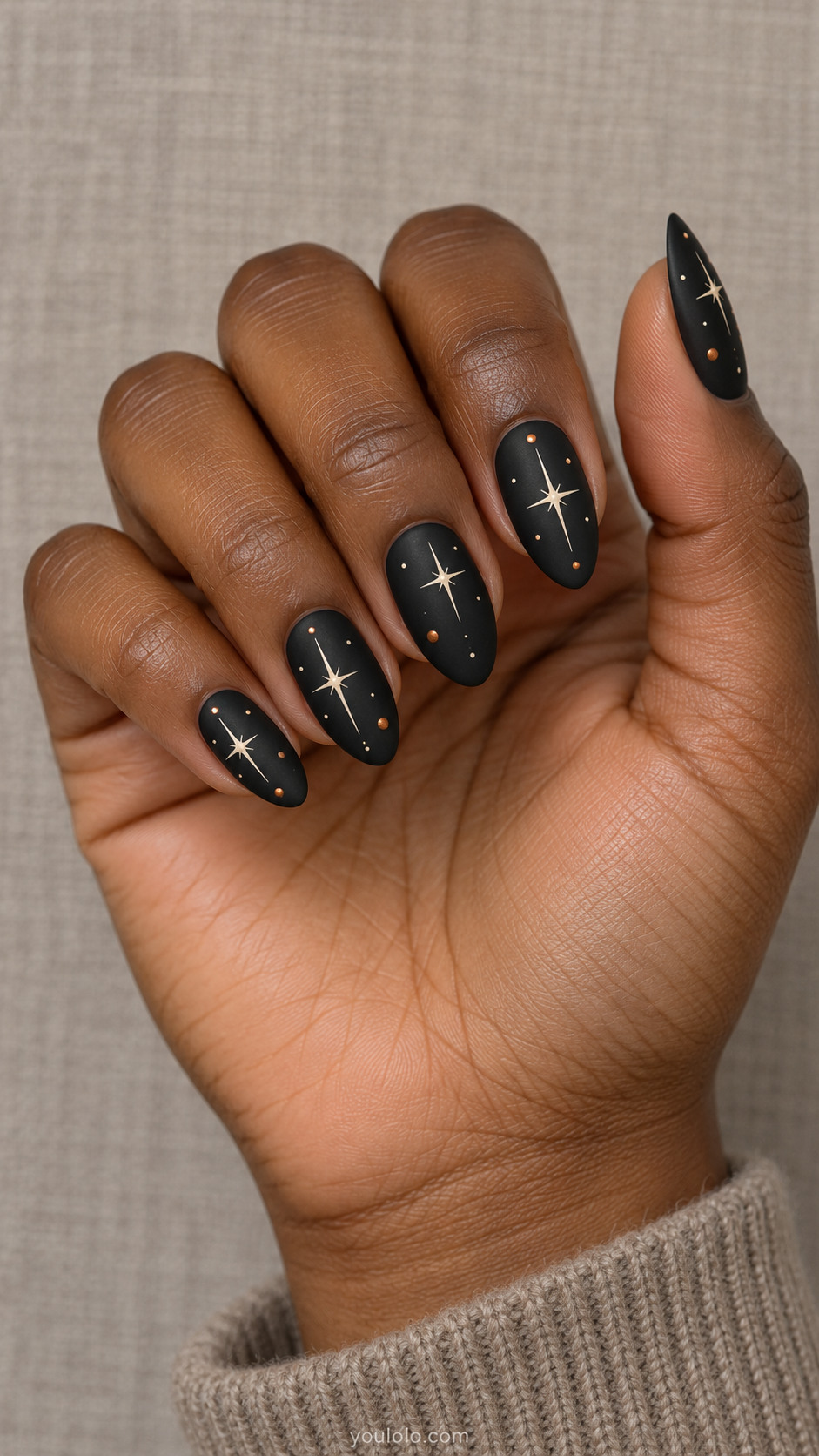 Matte black almond nails with ivory starbursts and sparse small copper dots