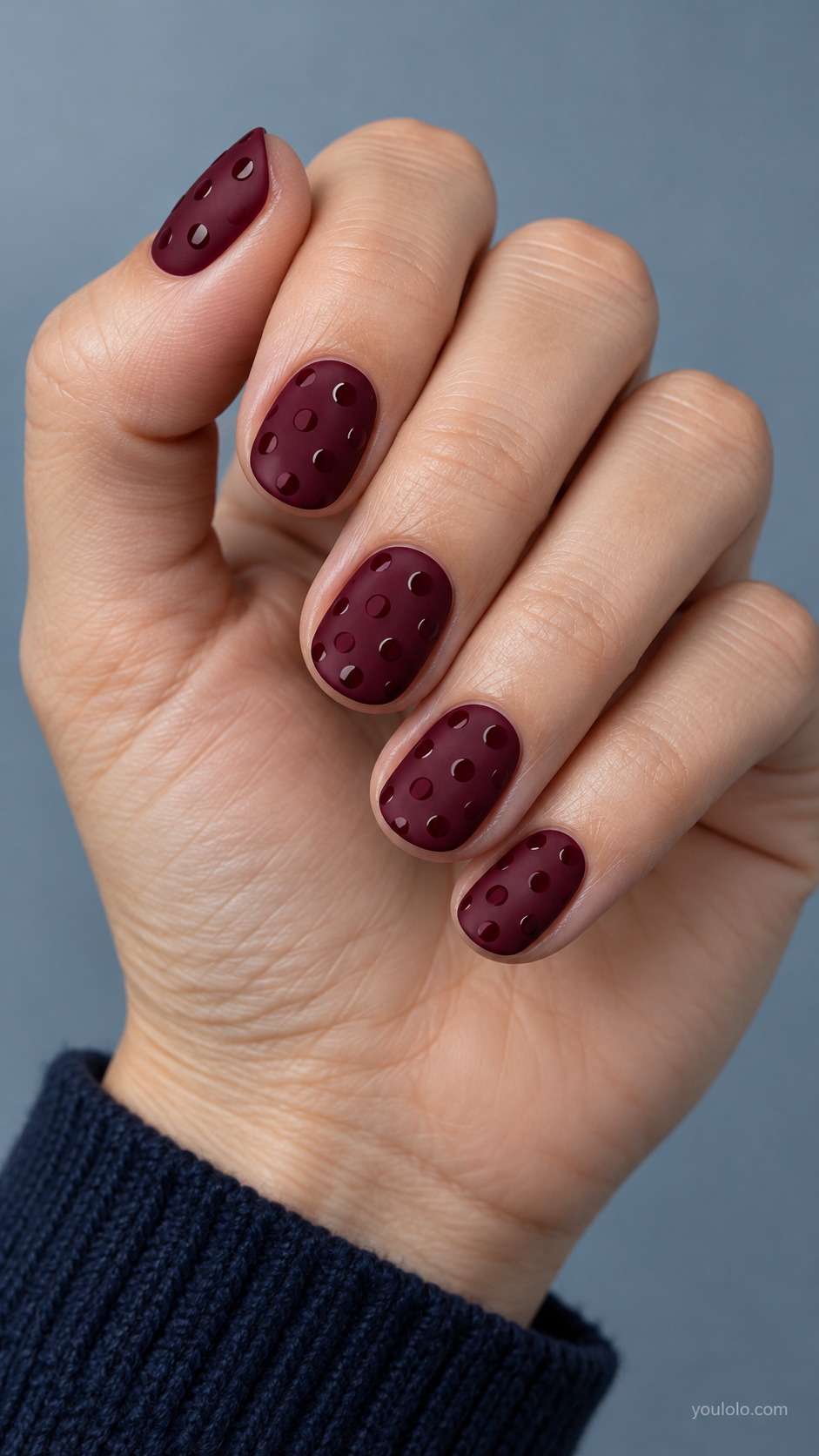 Short rounded burgundy nails matte velvet finish, slightly darker glossy burgundy evenly sized dots visible by subtle tiny reflections, no metallic.