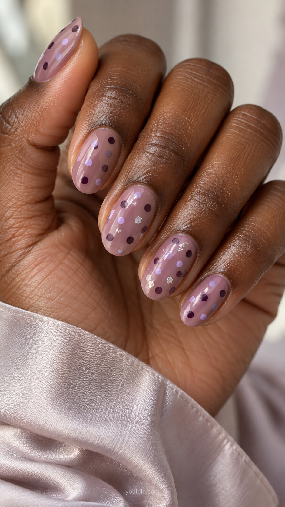 Mauve oval nails with purple dots and sparse silver foil flecks.