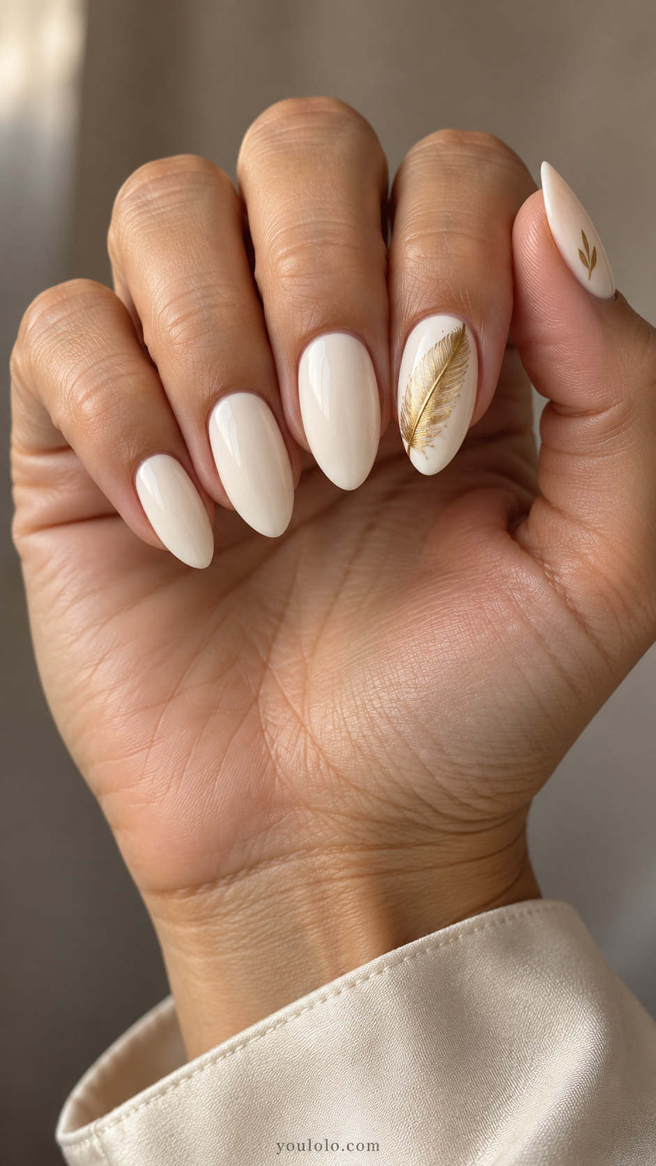 Medium almond ivory nails with a detailed gold feather on the index nail and a small thumb accent