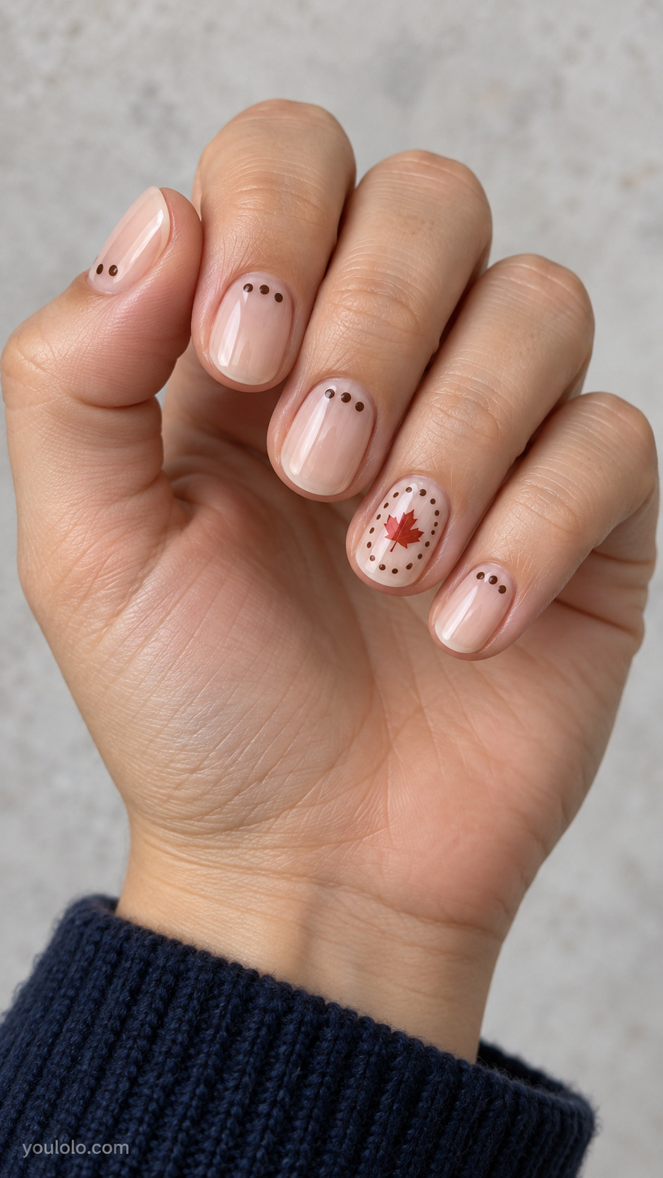 Short round nails with sheer beige nails, ring has one central tiny red maple leaf surrounded by a sparse oval of chocolate micro dots; other nails have three chocolate dots near cuticle.