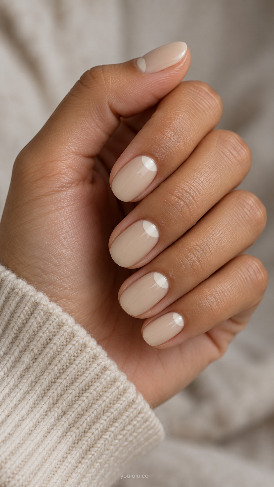 Short oval beige nails with small ivory half moons at the bases.