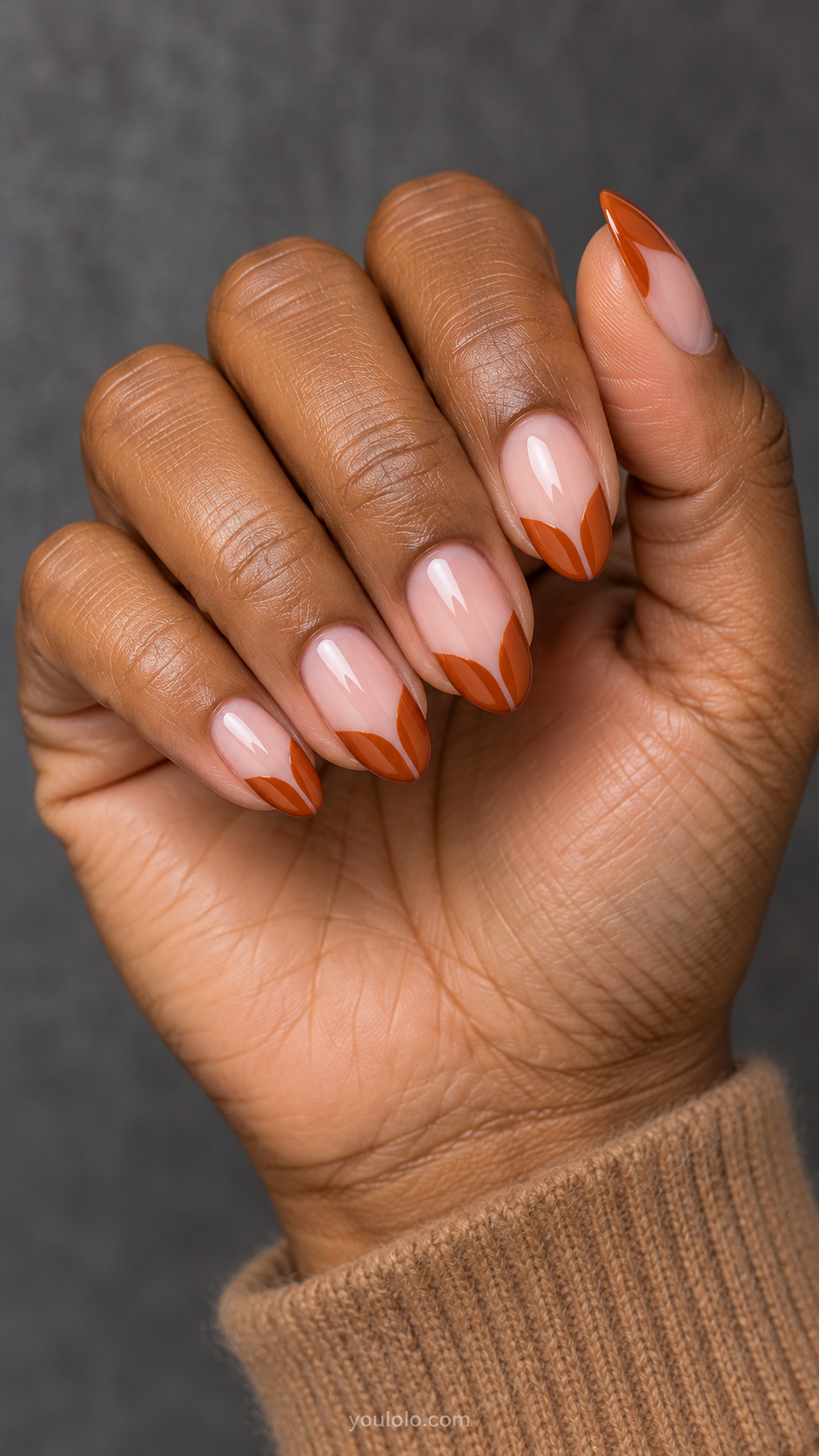 Medium oval nails with natural pink base with burnt orange French tips whose inner smile lines form two connected pointed leaf lobes with fine negative-space central slit, graphic leaf-tip silhouette.