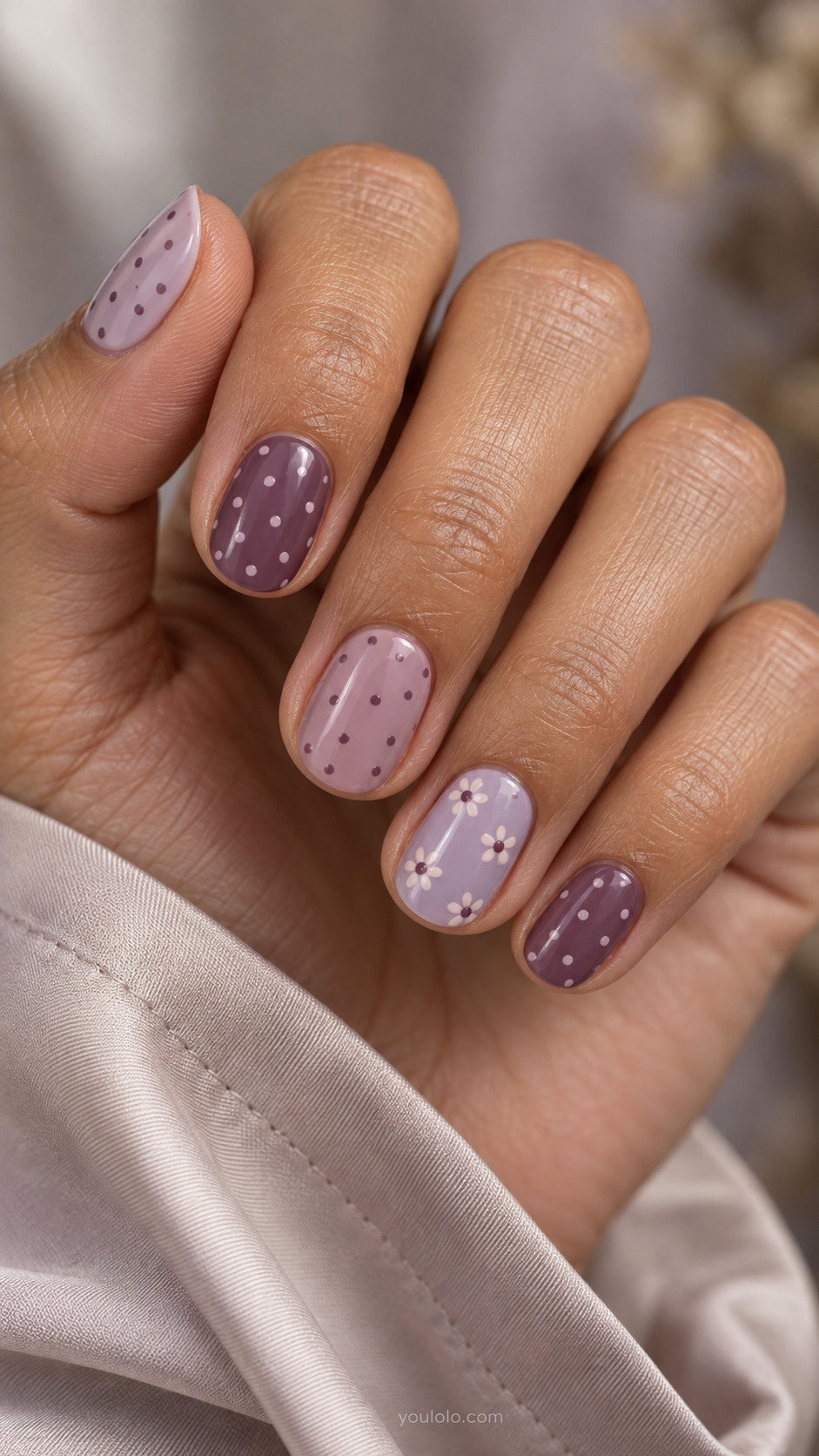 Short muted purple skittle nails with contrasting dots and ivory daisy accents.