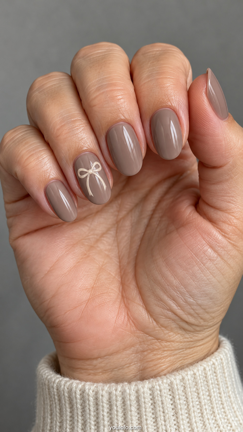 Medium oval nails: taupe nails, ring only small ivory gel-painted ribbon bow with two tapered tails, other nails plain taupe.
