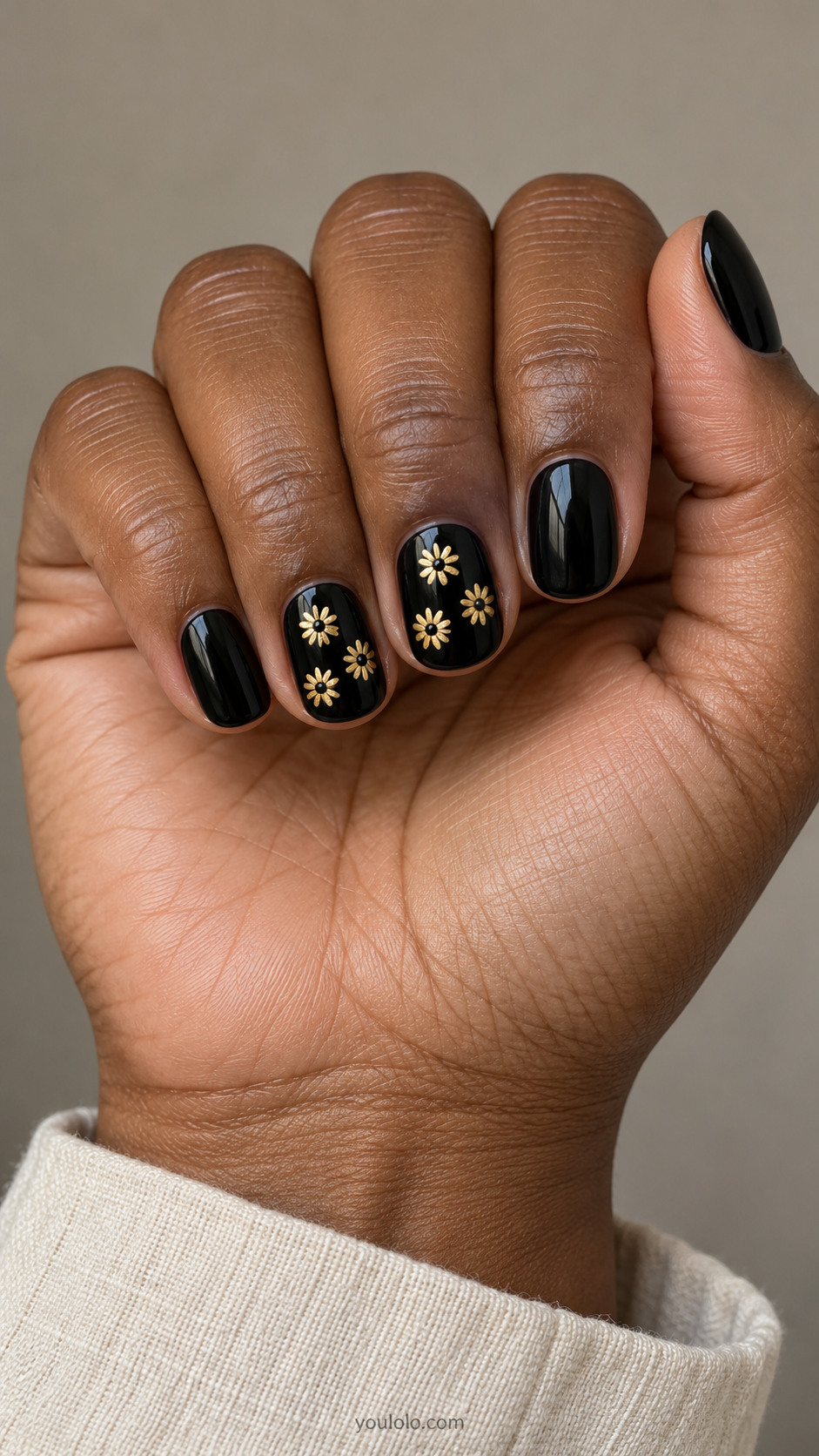 Short black nails with small gold daisies and black centers on accents