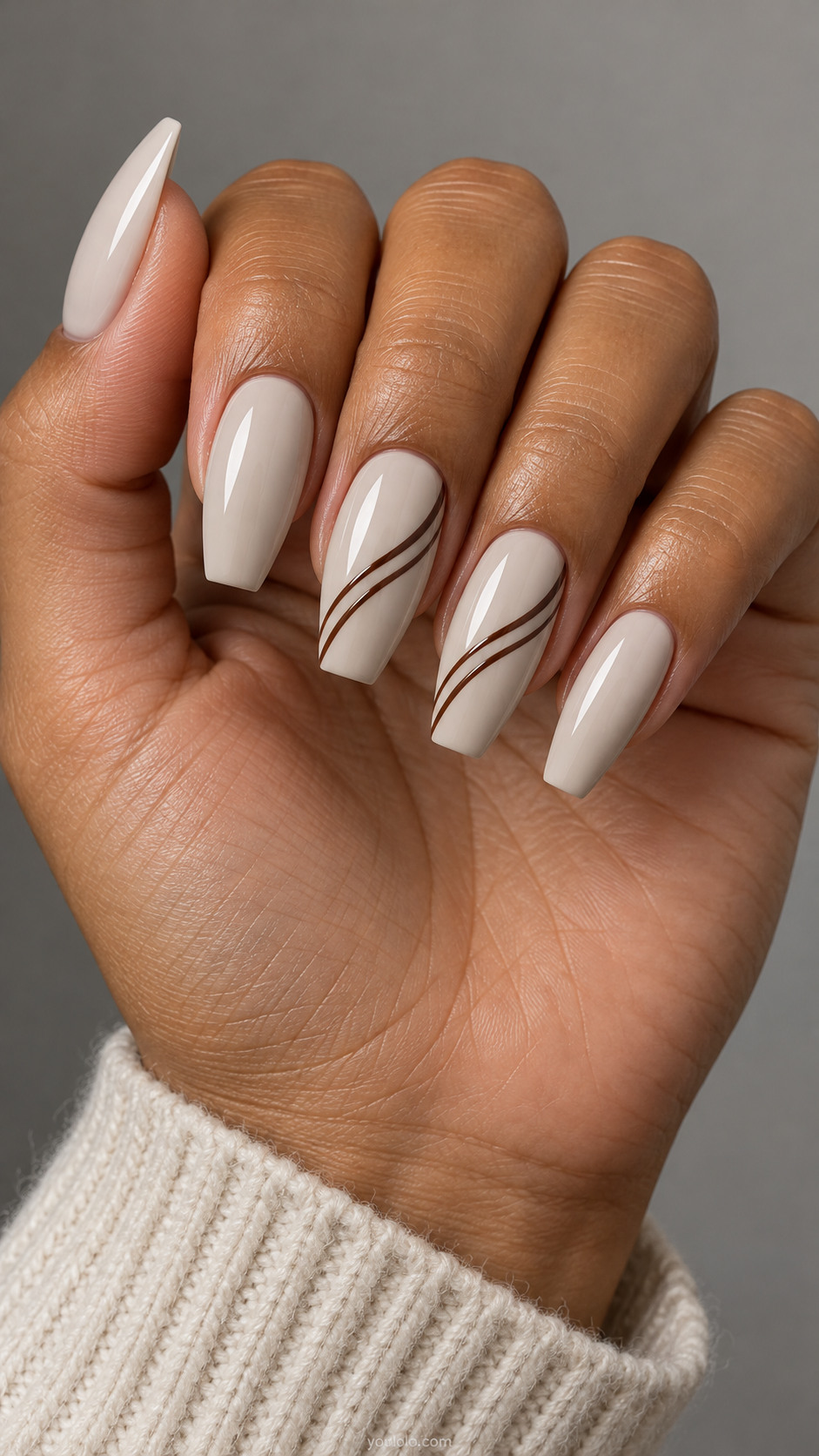 Long coffin nails: pale stone nails with two thin parallel espresso swoosh lines sweeping diagonally across middle and ring, remaining plain stone.