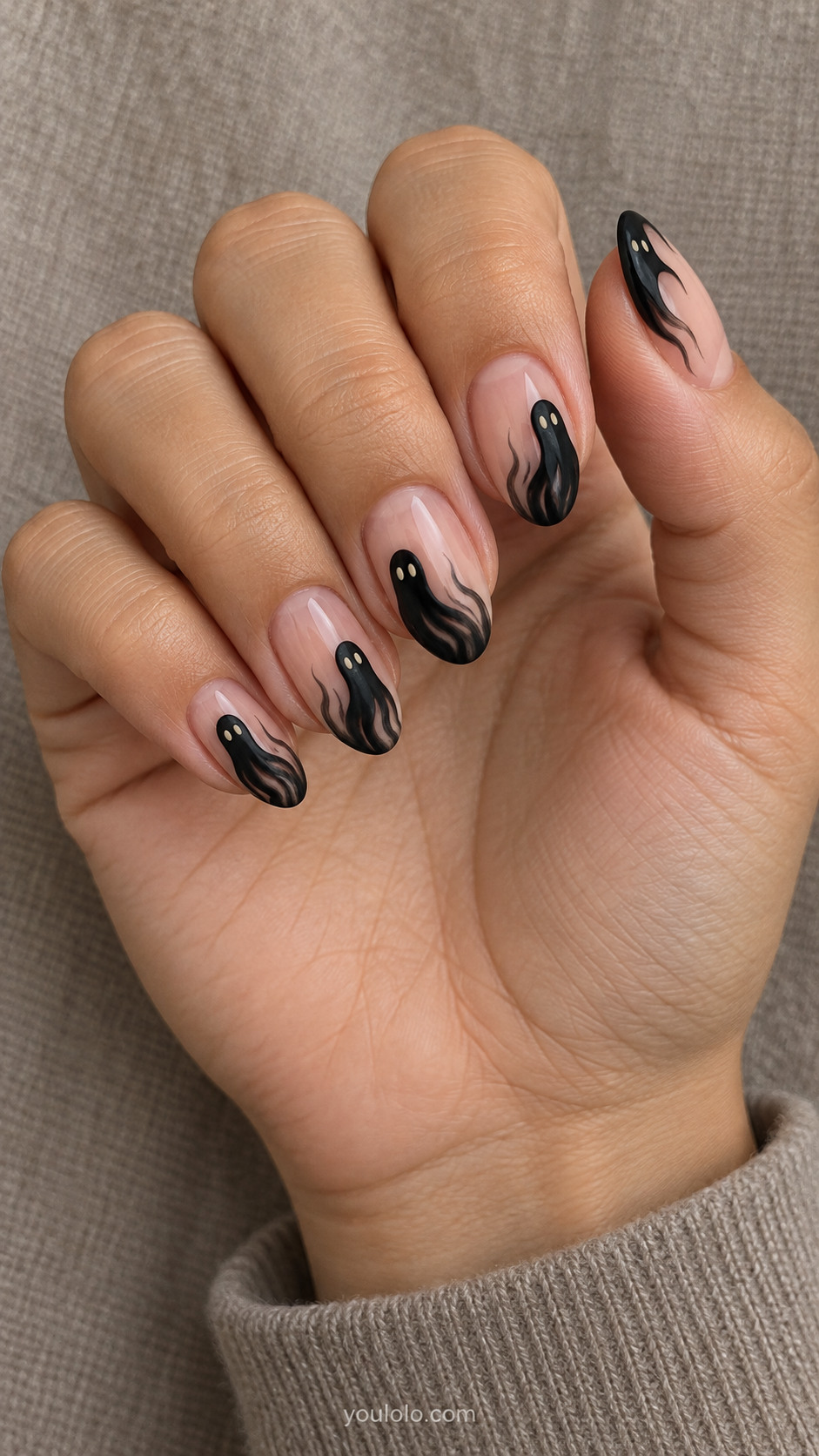 Medium oval sheer nude nails black ghost silhouettes rising from tips with curved wispy tails, two tiny cream eyes per ghost; uneven arty free edges