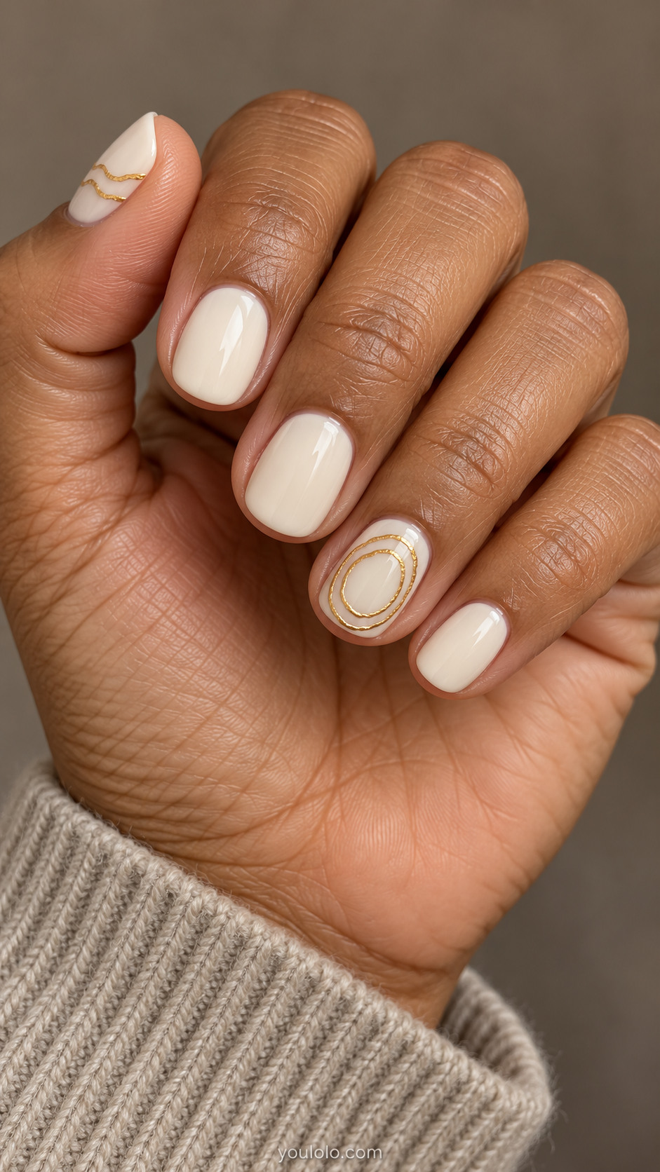 Short round ivory nails with two fine concentric gold rings on the ring nail and curved gold lines on the thumb