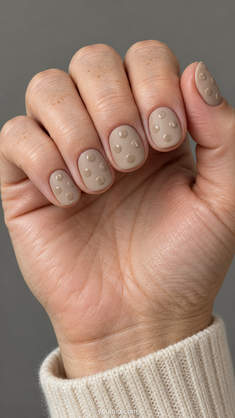 Short round nails: matte sand beige nails with four large spaced glossy same-color circles on each nail, finish contrast only.