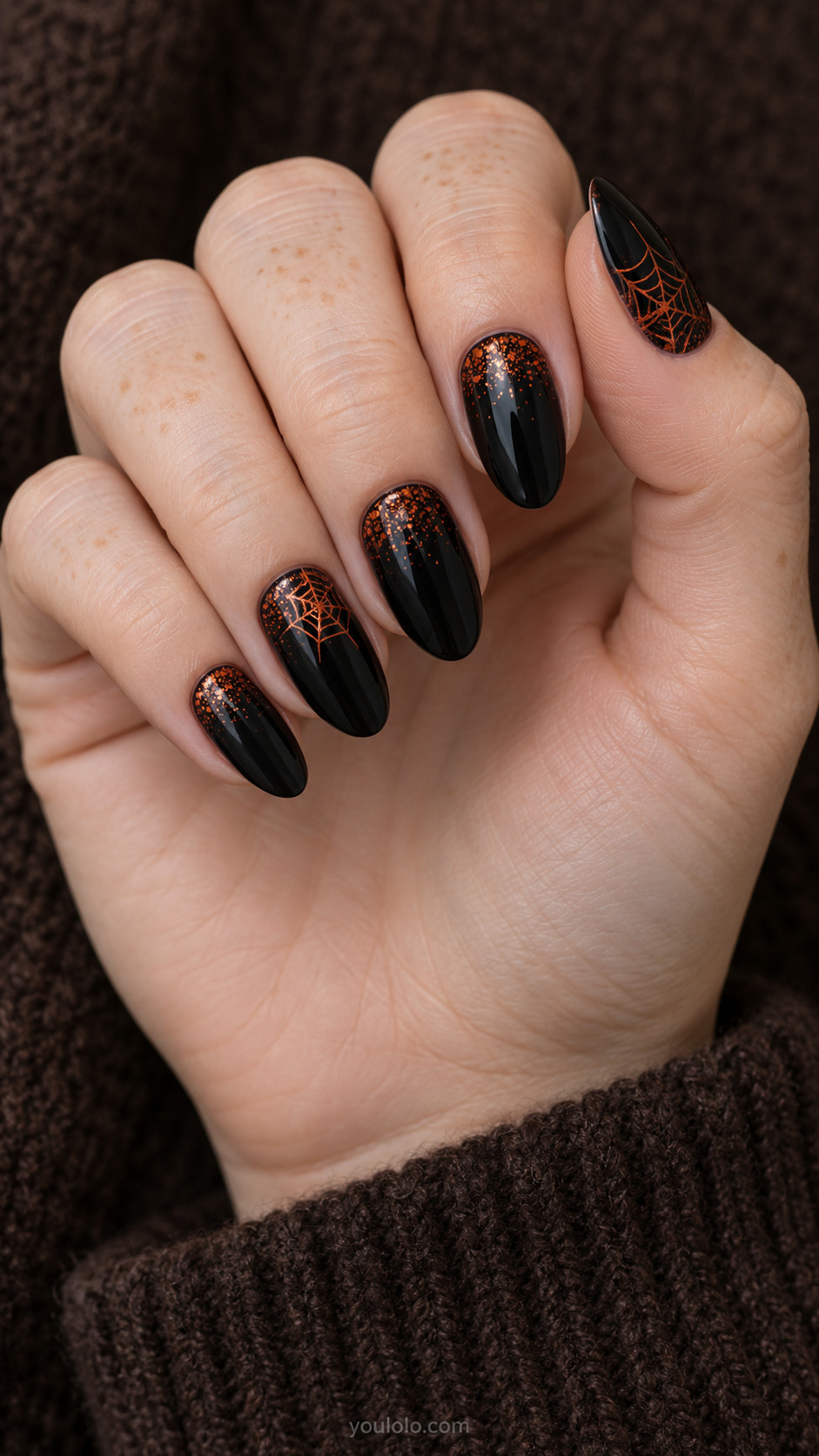 Medium almond black nails sparse burntorange fine ember dots clustered near cuticles fading to plain black tips, one small fine orange cobweb on thumb and ring