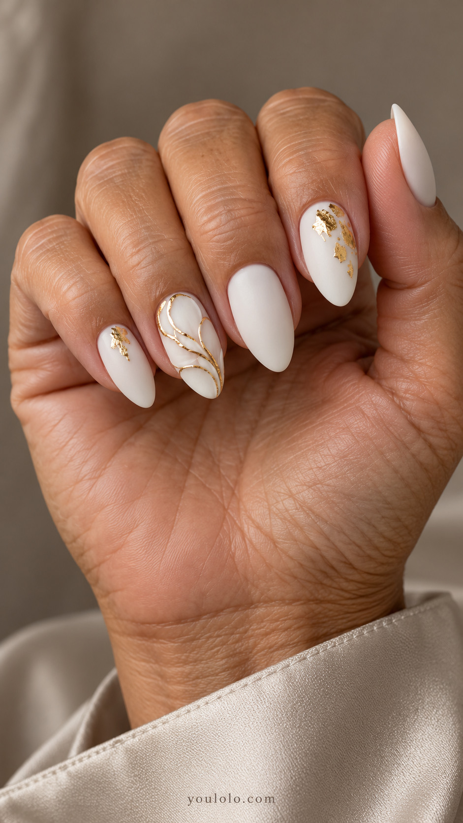 Medium almond matte-white nails with a low curved petal relief edged in gold on the ring nail and small foil accents on the index and little nails