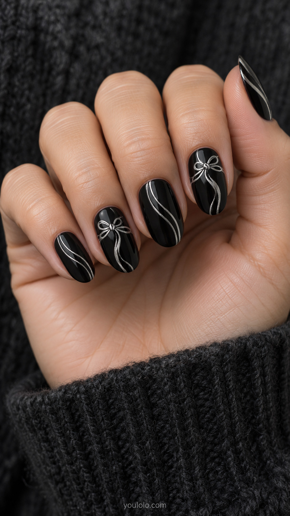 Glossy black oval nails with fine silver ribbon bows on two nails and curved silver trails on the others