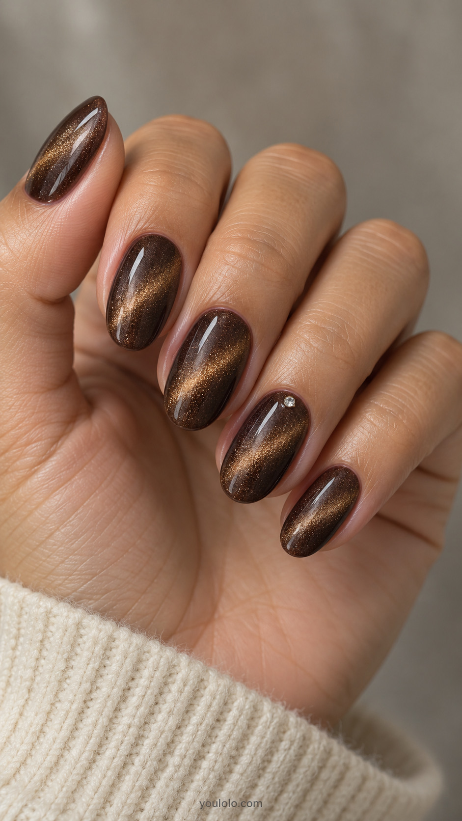 Medium oval nails: deep brown magnetic diagonal bronze bands all nails; ring one tiny clear round low-profile crystal near cuticle, no other ornaments.