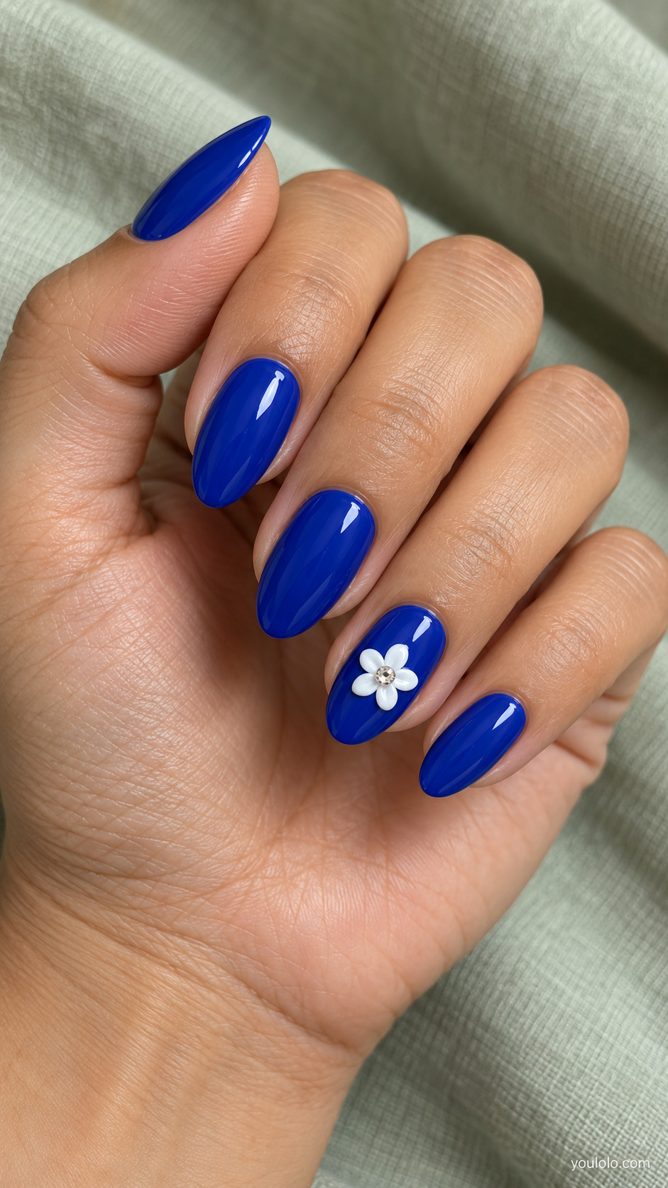 Royal blue almond nails with one raised white flower and a crystal center