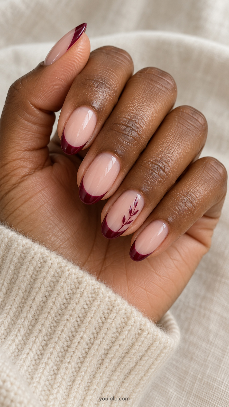 medium oval nude nails, dark wine red French tips, one tiny delicate painted wine-red leafy branch along side of ring nail on a naturally gathered hand