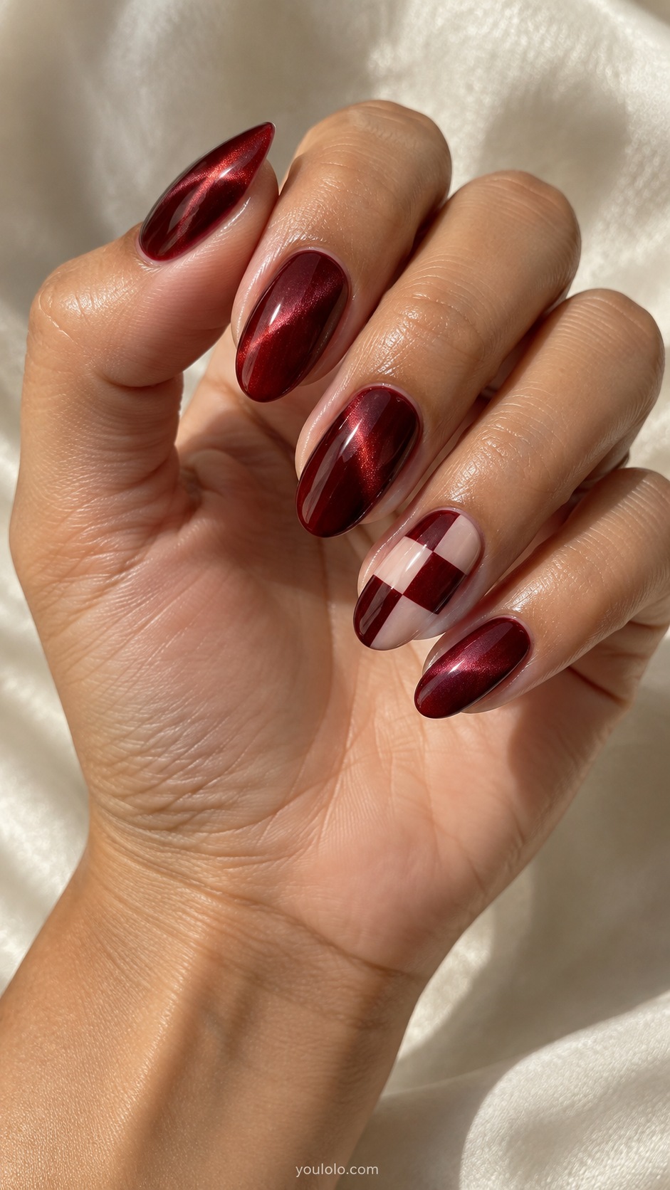 Garnet with a Checker Accent cat eye nails — Medium almond garnet red magnetic nails with one ring nail checker pattern deep burgundy and sheer nude, four by three large squares.